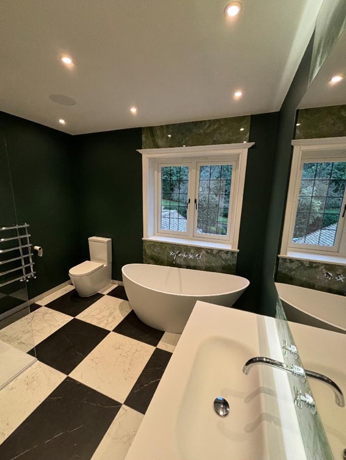 Dark green bathroom with green marble, chequerboard marble floor and freestanding bath