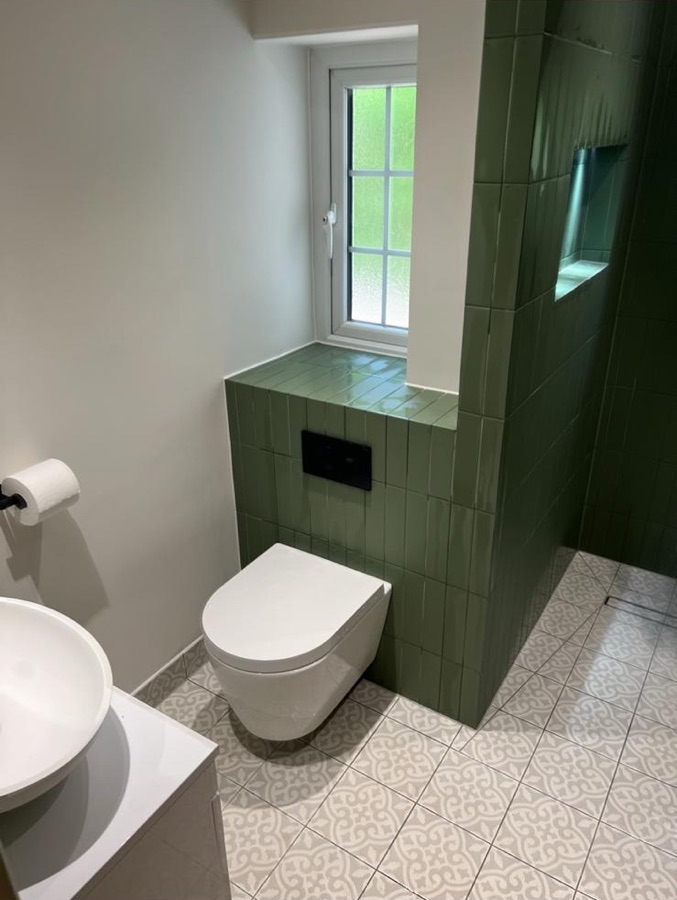 Olive green tiled cistern wall, wall-hung WC and patterned floor tiles