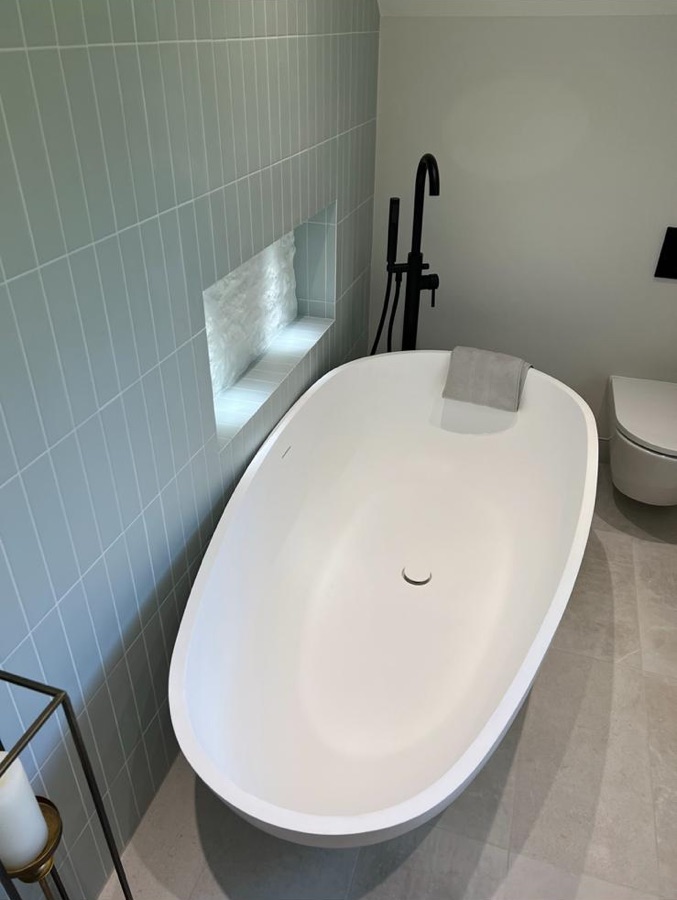 Freestanding bath with sage green vertical tiles and a lit niche